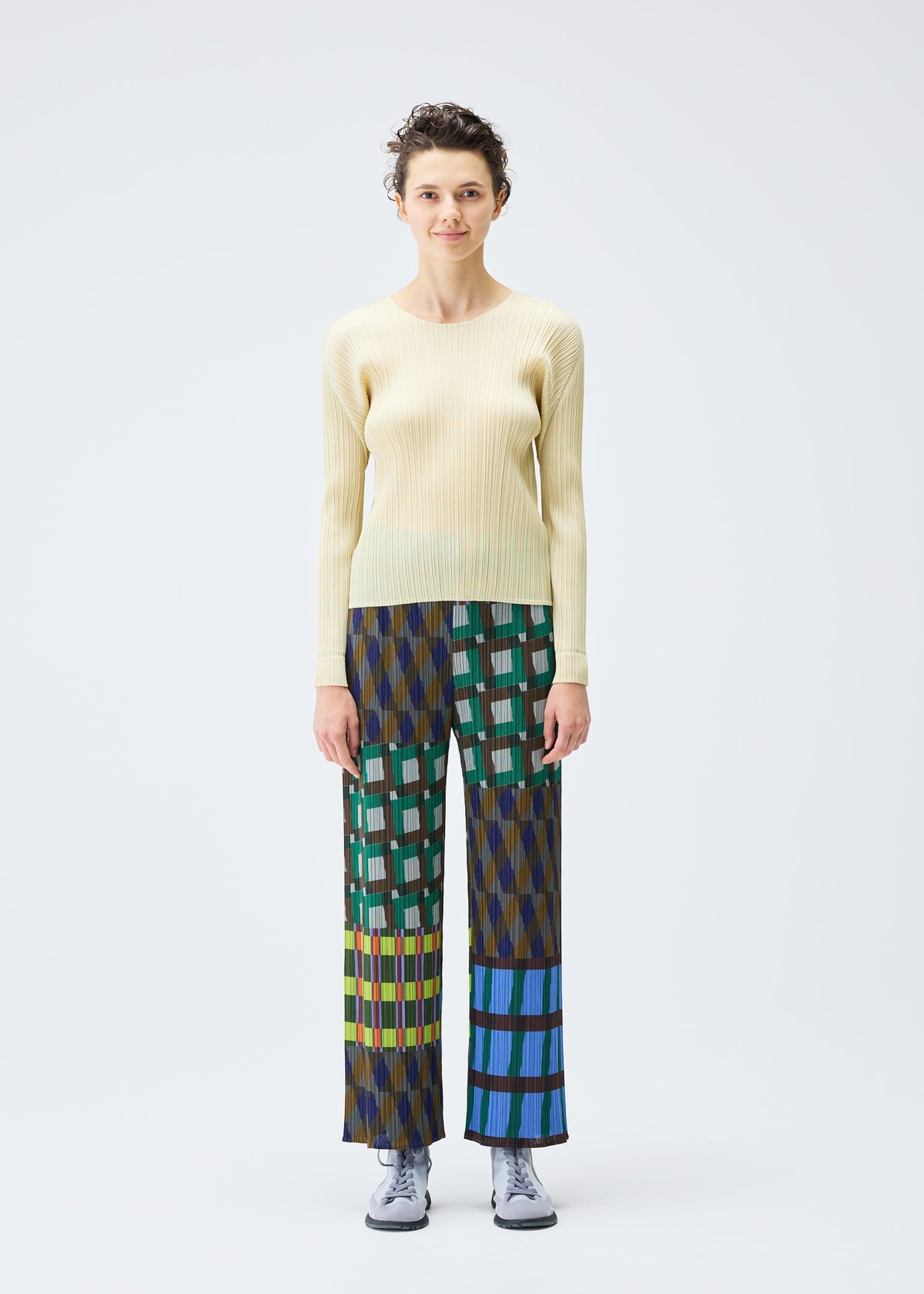 A person stands facing forward against a white background, wearing HARMONY wide-leg geometric pants and a pale yellow ribbed sweater by PLEATS PLEASE ISSEY MIYAKE, paired with light gray lace-up shoes. view 4 of 6
