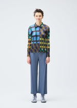 A person stands facing forward, wearing the HARMONY long-sleeved shirt and loose blue pleated pants by PLEATS PLEASE ISSEY MIYAKE, paired with light-colored shoes, against a plain white background.