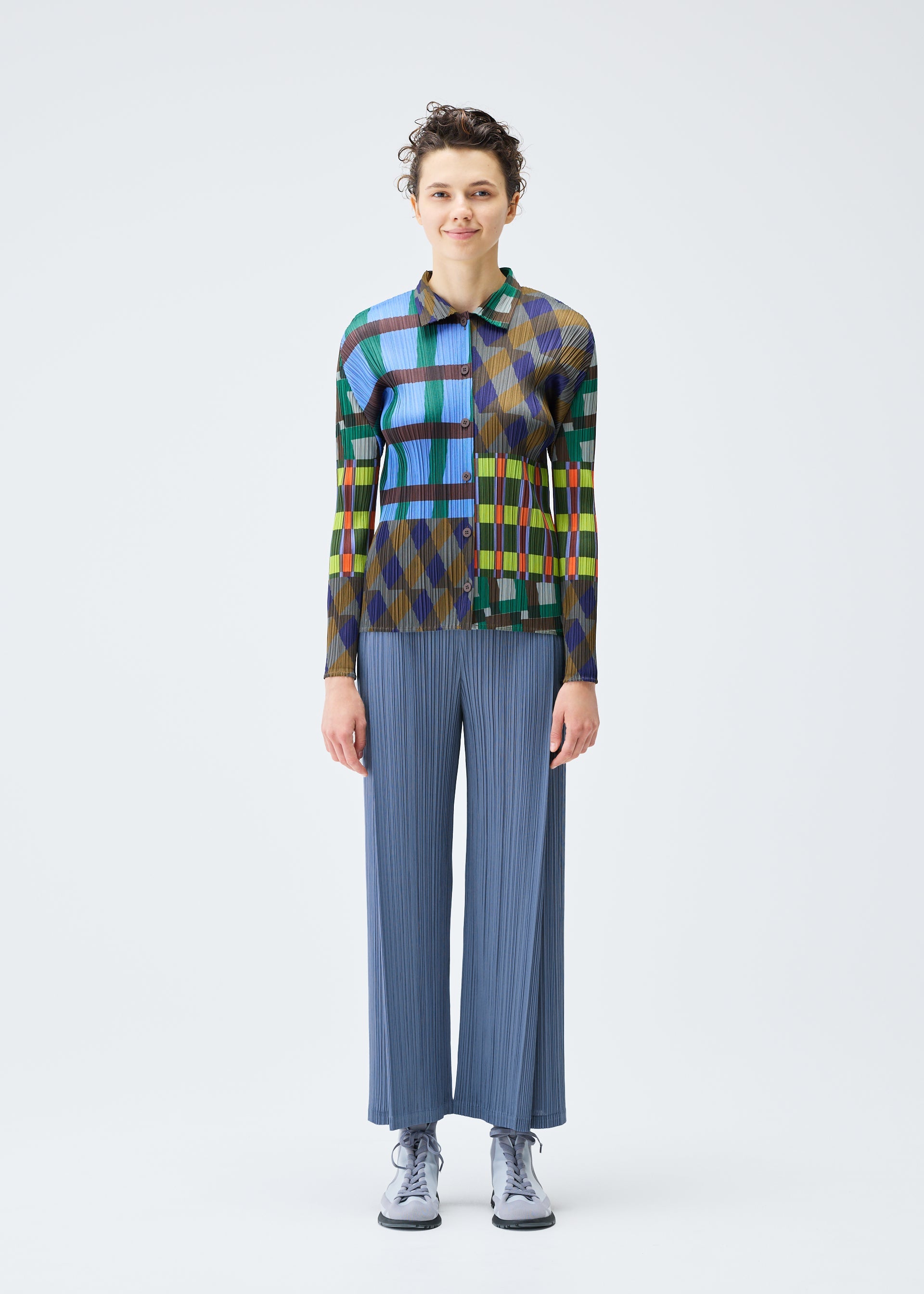 Zoomed view A person stands facing forward, wearing the HARMONY long-sleeved shirt and loose blue pleated pants by PLEATS PLEASE ISSEY MIYAKE, paired with light-colored shoes, against a plain white background.