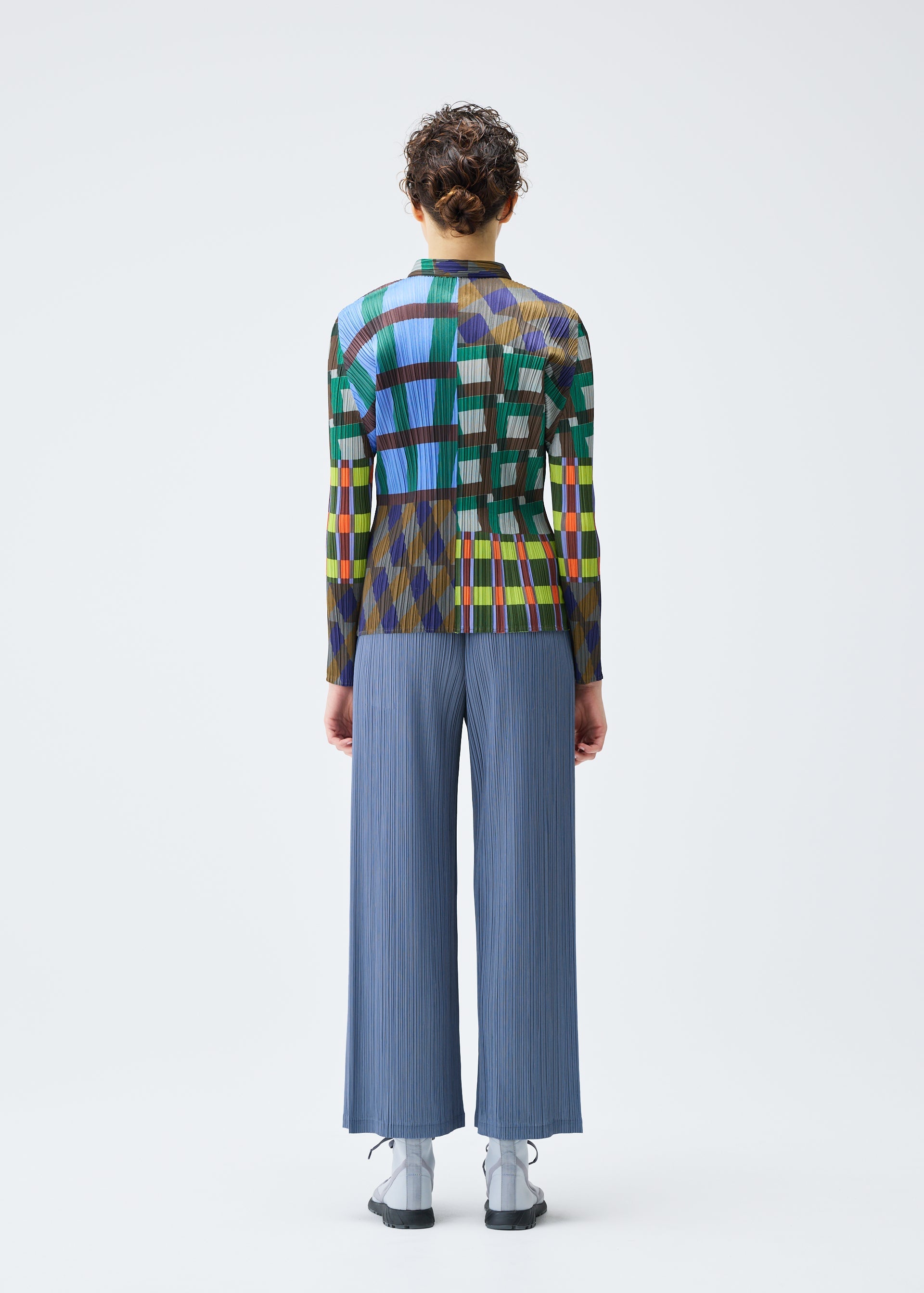 Zoomed view A person with short curly hair stands facing away, wearing the HARMONY long-sleeved geometric print shirt and loose light blue pleated pants by PLEATS PLEASE ISSEY MIYAKE, paired with light gray shoes against a white background.
