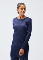 A person with cornrow braids smiles and looks to the side, wearing the dark blue TUNE round-neck tunic by PLEATS PLEASE ISSEY MIYAKE, featuring vertical pleats, against a plain light background.