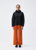 A person stands against a plain white background wearing the A-POC SHELL turtleneck sweater and bright orange wide-leg pleated pants by PLEATS PLEASE ISSEY MIYAKE, paired with black shoes, looking straight ahead with a neutral expression.