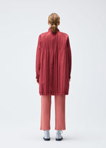 A person with light brown hair in a low ponytail faces away, wearing the PADDED PLEATS COAT by PLEATS PLEASE ISSEY MIYAKE over pleated pink pants and black shoes, set against a plain white background.