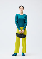 A woman stands against a white background wearing a teal, long-sleeved, horizontally pleated top, bright yellow pleated pants, blue shoes, and holding the PLEATS BOSTON BAG by PLEATS PLEASE ISSEY MIYAKE.