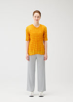 A person faces forward against a white background, wearing the TWISTED BORDER SHIRT by PLEATS PLEASE ISSEY MIYAKE in yellow, paired with light gray wide-leg pants and white sneakers.