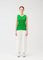 A person stands against a white background wearing the MIST APRIL sleeveless tank top in green by PLEATS PLEASE ISSEY MIYAKE, paired with wide-leg white pants and white sneakers, facing forward with a neutral expression.