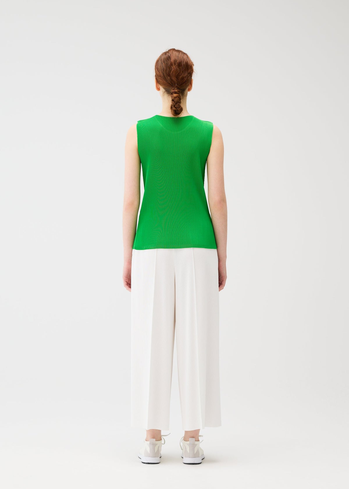 A person with red braided hair, wearing the MIST APRIL outfit by PLEATS PLEASE ISSEY MIYAKE—sleeveless tank top, wide white pants, and white shoes—stands facing away against a plain white background. view 7 of 8