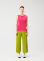 A woman faces forward against a white background, wearing the MIST JUNE bright pink tank top and lime green pleated wide-leg pants by PLEATS PLEASE ISSEY MIYAKE, styled with white sneakers and a neutral expression.