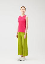 A person smiles in MIST JUNE by PLEATS PLEASE ISSEY MIYAKE: a bright pink lightweight tank top and wide-leg lime green pants, styled with white sneakers, posed against a plain white background.