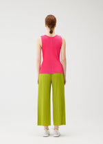 A person with tied-back hair faces away, wearing the MIST JUNE sleeveless bright pink top and lime green pleated wide-leg pants by PLEATS PLEASE ISSEY MIYAKE, paired with white sneakers against a plain white background.