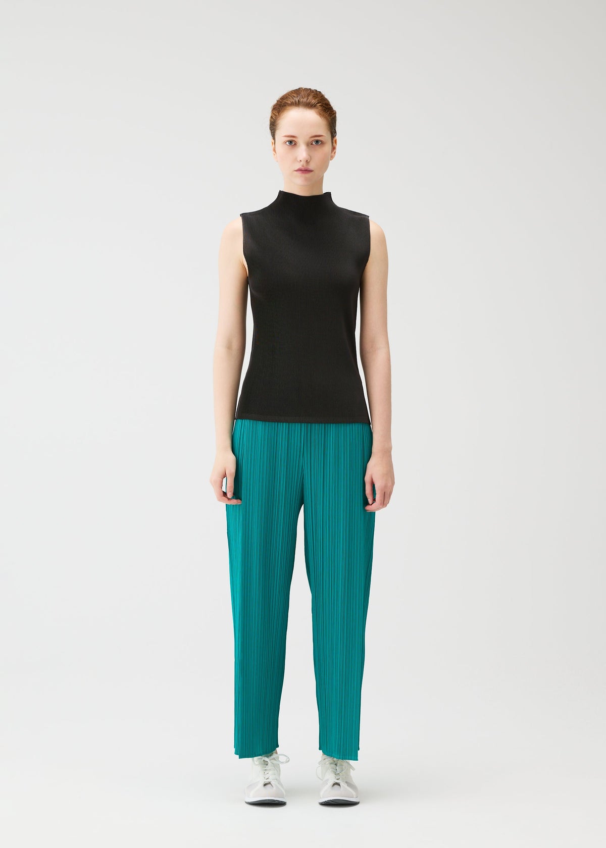 A person faces forward against a plain white background, dressed in the MIST JUNE top and fine pleats teal pants by PLEATS PLEASE ISSEY MIYAKE, paired with white sneakers. view 5 of 7