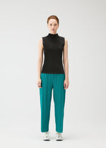 A person faces forward against a plain white background, dressed in the MIST JUNE top and fine pleats teal pants by PLEATS PLEASE ISSEY MIYAKE, paired with white sneakers.