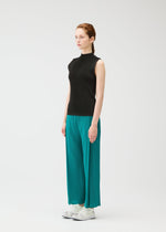 A woman with light skin and reddish-brown braids wears the MIST JUNE high-neck sleeveless top and teal pleated wide-leg pants by PLEATS PLEASE ISSEY MIYAKE, styled with white sneakers, against a plain white background.