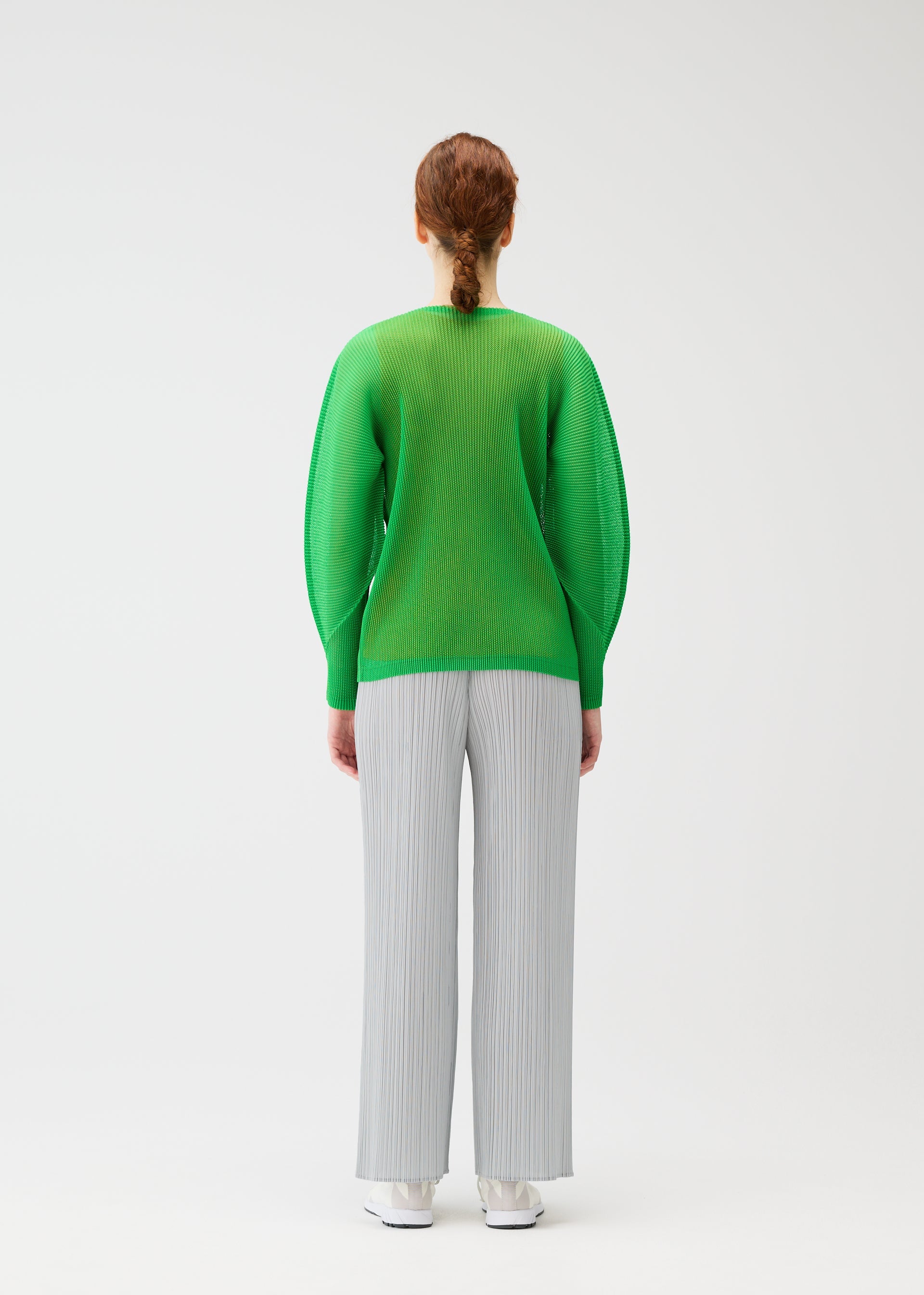 Zoomed view A person with red hair in a low braid, seen from behind, wears the bright green TATAMI APRIL pleated top with dolman sleeves by PLEATS PLEASE ISSEY MIYAKE and light gray wide-leg pants against a plain white background.