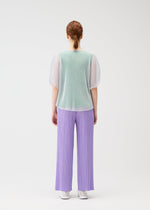 A person with red hair in a low braid faces away, modeling the TATAMI APRIL by PLEATS PLEASE ISSEY MIYAKE: a sheer mint green mesh top, loose pleated lavender pants, and white shoes against a plain white background.