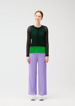 A person stands against a plain white background, smiling, wearing the TATAMI APRIL pleated pants by PLEATS PLEASE ISSEY MIYAKE in light purple, paired with a black and green mesh long-sleeve top and white sneakers.