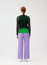 A person with red hair in a low braid faces away, wearing wide lilac TATAMI APRIL pants by PLEATS PLEASE ISSEY MIYAKE, black mesh long-sleeve top, green shirt, and white sneakers against a plain white background.
