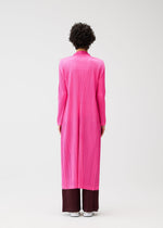 A person with short curly hair stands facing away, wearing the MONTHLY COLORS : JANUARY bright pink pleated coat by PLEATS PLEASE ISSEY MIYAKE over dark brown wide-leg pants and white shoes, against a plain white background.