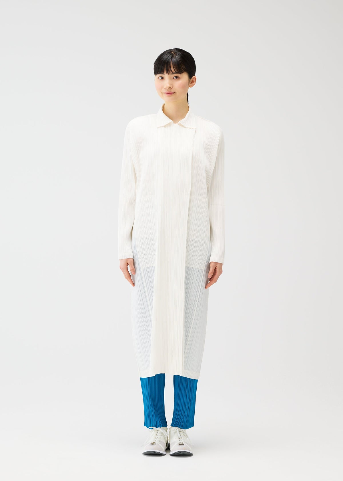 A person stands facing forward in a straight silhouette, wearing PLEATS PLEASE ISSEY MIYAKE’s MONTHLY COLORS : FEBRUARY—a sheer, white collared long coat over bright blue pleated pants and white shoes—against a plain white background. view 8 of 12