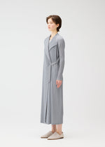 A person stands sideways in the FACADE robe by PLEATS PLEASE ISSEY MIYAKE—long, light gray, pinstriped with a cord belt and matching slippers—against a plain white background.