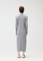 A person with short brown hair faces away, wearing the FACADE long, light gray pleated dress from PLEATS PLEASE ISSEY MIYAKE under a subtly corded long coat, with beige flats, against a plain white background.
