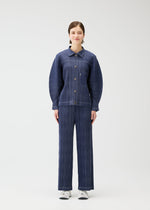 A person stands facing forward in a matching blue COTTON DENIM collared jacket and pants from PLEATS PLEASE ISSEY MIYAKE, paired with white sneakers, set against a plain light background.