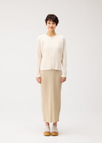 A person faces forward against a white background, wearing the cream-colored STARDUST textured cardigan and beige pleated skirt by PLEATS PLEASE ISSEY MIYAKE, styled with beige platform sandals.