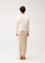 A person with short dark hair faces away, wearing the PLEATS PLEASE ISSEY MIYAKE STARDUST beige pleated midi skirt, a cream knit sweater with a voluminous fit, and tan platform sandals against a plain light background.