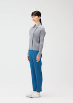A woman with long dark hair stands in profile wearing the MONTHLY COLORS : FEBRUARY ribbed cardigan and blue pleated pants from PLEATS PLEASE ISSEY MIYAKE, paired with white sneakers against a plain white background.