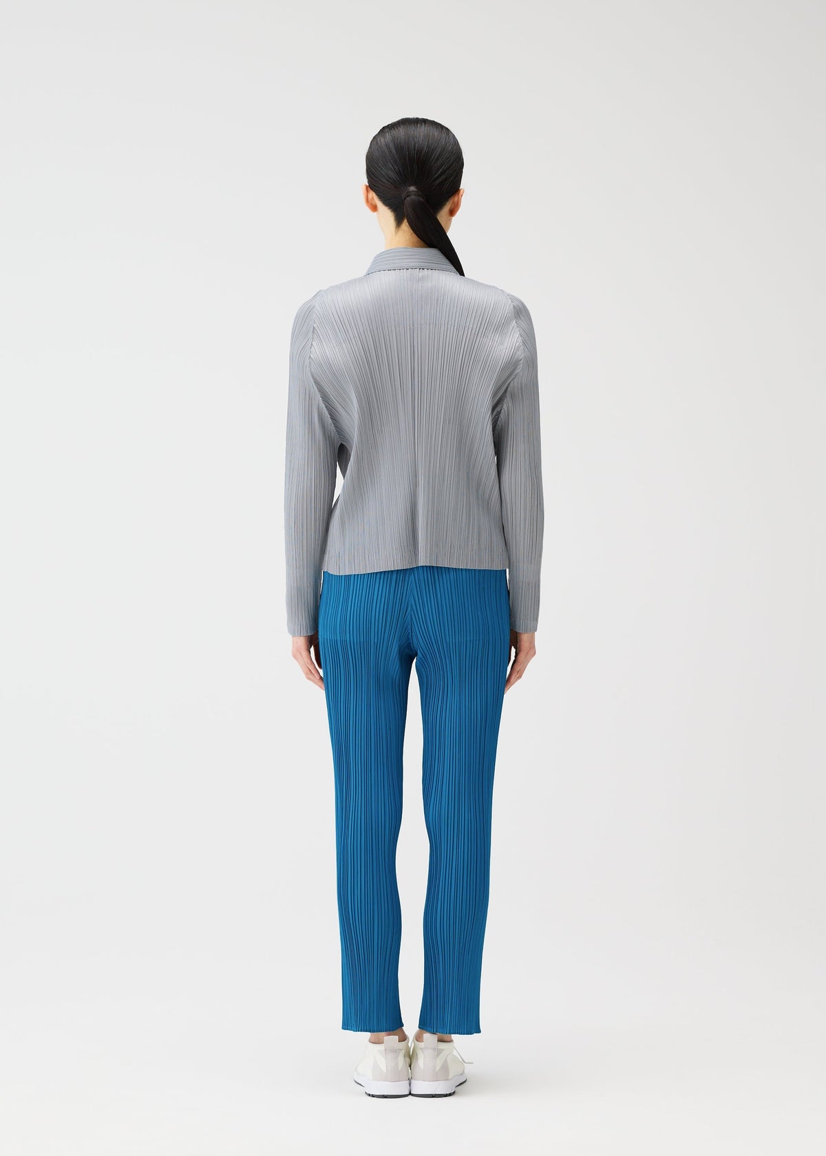 A person faces away, wearing a light gray long-sleeved pleated top and bright blue pleated pants from PLEATS PLEASE ISSEY MIYAKE's MONTHLY COLORS : FEBRUARY, paired with white shoes against a plain white background. view 10 of 11