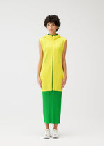 A person with short curly hair stands against a white background, wearing the MONTHLY COLORS : APRIL sleeveless yellow textured top and bright green skirt from PLEATS PLEASE ISSEY MIYAKE, paired with white sneakers.