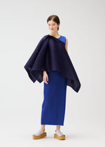 A woman models the LUCID PLEATS sleeveless blue dress by PLEATS PLEASE ISSEY MIYAKE, paired with beige platform sandals. She drapes a 3D dark blue pleated shawl over one shoulder and smiles softly against a white background.