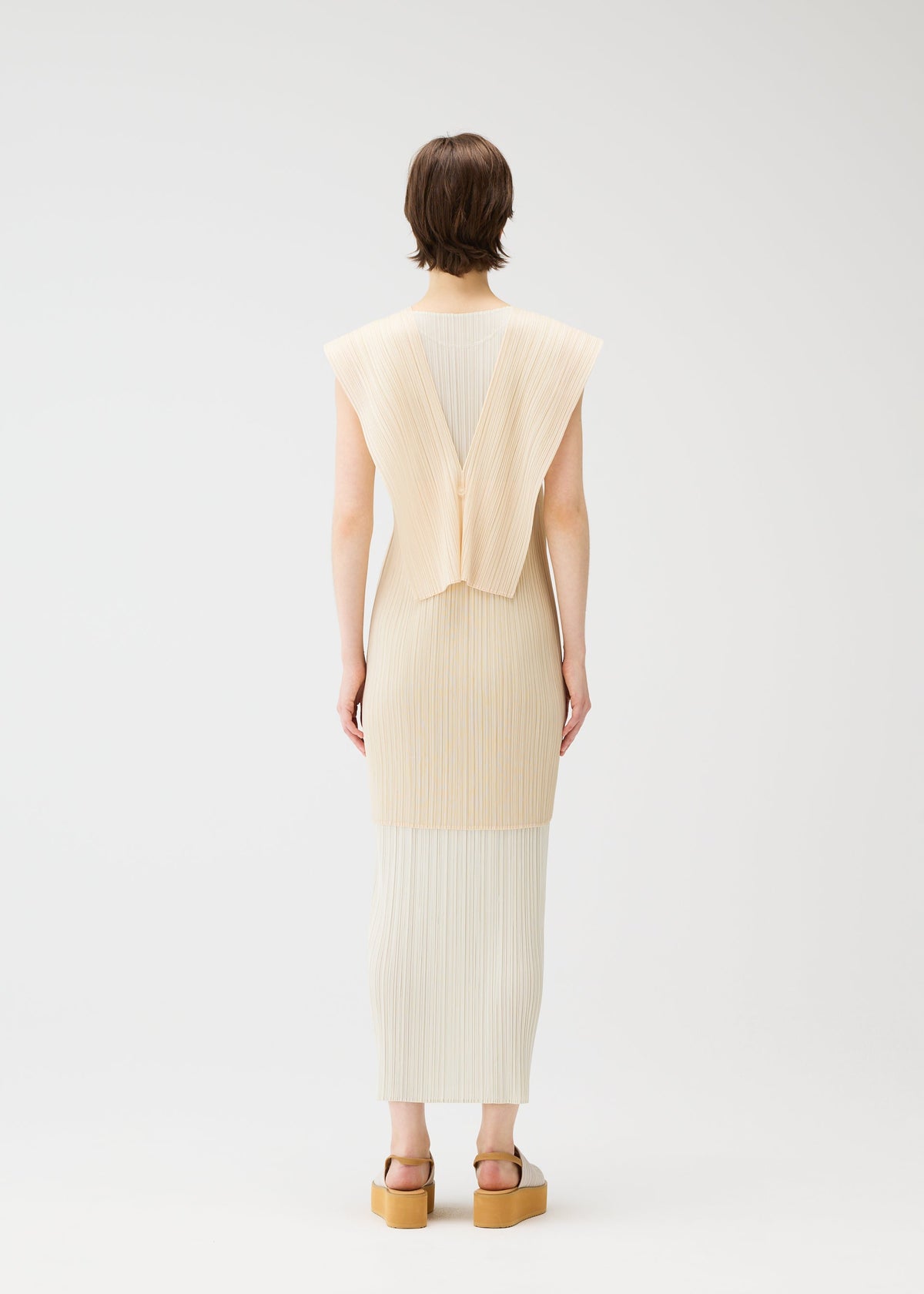 A person faces away wearing the LUCID PLEATS sleeveless cream dress by PLEATS PLEASE ISSEY MIYAKE, featuring pleats and a geometric back detail, paired with tan platform sandals. Style with a sheer long vest. Background is plain white. view 7 of 9