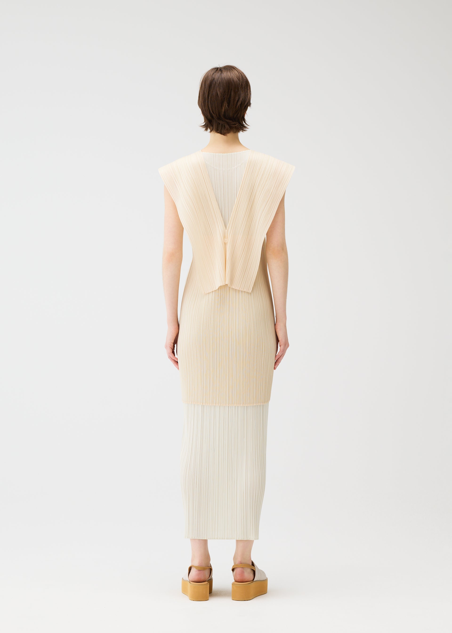 Zoomed view A person faces away wearing the LUCID PLEATS sleeveless cream dress by PLEATS PLEASE ISSEY MIYAKE, featuring pleats and a geometric back detail, paired with tan platform sandals. Style with a sheer long vest. Background is plain white.