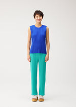 A person with short dark hair smiles while wearing the STARDUST sleeveless blue top by PLEATS PLEASE ISSEY MIYAKE, paired with loose teal pants and tan platform sandals, standing against a plain light background.