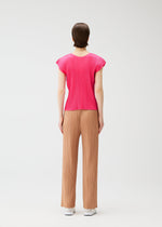 A person stands facing away, wearing the MONTHLY COLORS : JUNE pink pleated top and loose tan pants with side pockets from PLEATS PLEASE ISSEY MIYAKE, paired with white shoes, against a plain white background.