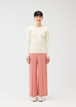 A woman stands against a white background, wearing the RAMIE PLEATS wide pants by PLEATS PLEASE ISSEY MIYAKE, paired with a cream ribbed long-sleeve top and light pink shoes. She faces forward, arms relaxed at her sides.