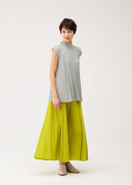 A woman with short brown hair wears the MELLOW PLEATS sleeveless light gray top and bright yellow long skirt from PLEATS PLEASE ISSEY MIYAKE, standing against a plain white background and looking to the side with a slight smile.