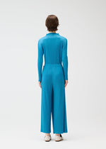 A person with short brown hair is seen from behind, wearing the FACADE blue pleated wide-leg jumpsuit by PLEATS PLEASE ISSEY MIYAKE and white flat shoes, set against a plain light background.