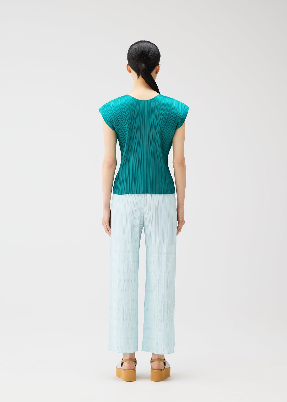 A woman with straight black hair tied back wears PLEATS PLEASE ISSEY MIYAKE's BUMPY BASKET: a teal pleated cap-sleeve top and light blue plaid straight pants with side pockets, plus beige platform sandals, against a plain white background. view 7 of 8