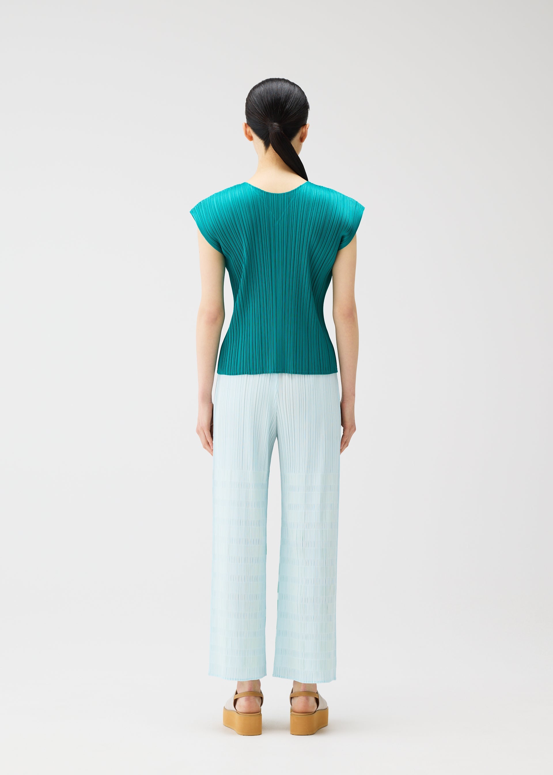 Zoomed view A woman with straight black hair tied back wears PLEATS PLEASE ISSEY MIYAKE's BUMPY BASKET: a teal pleated cap-sleeve top and light blue plaid straight pants with side pockets, plus beige platform sandals, against a plain white background.
