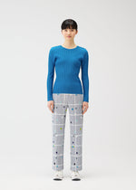 A woman faces forward in PLEATS PLEASE ISSEY MIYAKE's CROSSING DOTS straight pants with a plaid and dots grid pattern, a fitted blue ribbed long-sleeve top, and white sneakers against a plain white background.