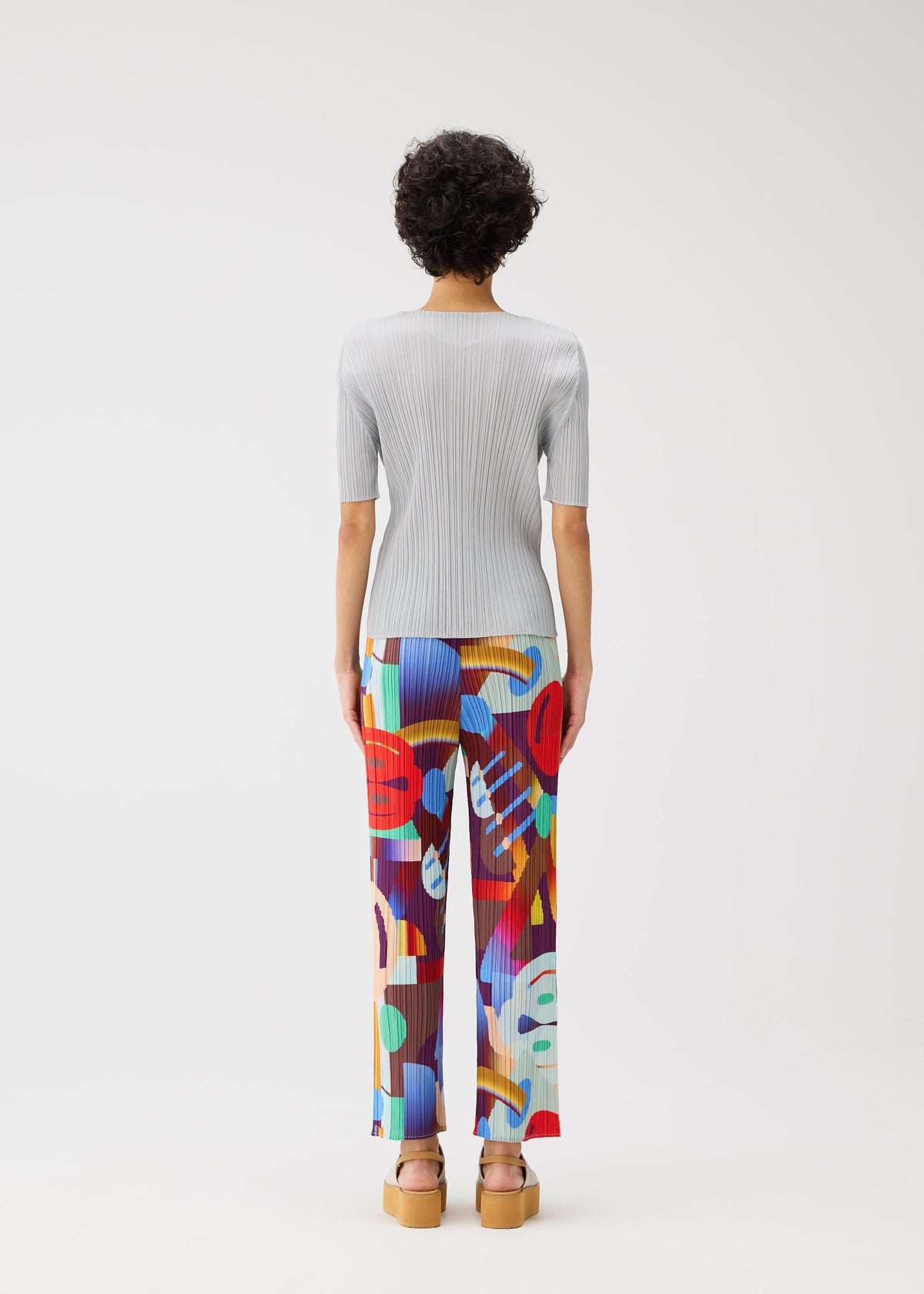 Facing away, a person with short curly hair wears the PLAYGROUND ribbed top and colorful geometric pants by PLEATS PLEASE ISSEY MIYAKE, styled with tan platform sandals against a plain white background. view 6 of 7