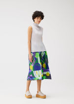 A woman with short curly hair models the PLAYGROUND pleated top and playful printed midi skirt from PLEATS PLEASE ISSEY MIYAKE, styled with neutral platform sandals against a plain white background.