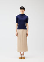 A woman faces forward against a plain light background, wearing a navy ribbed top and beige pleated skirt from the MONTHLY COLORS : MAY collection by PLEATS PLEASE ISSEY MIYAKE, paired with beige platform sandals.