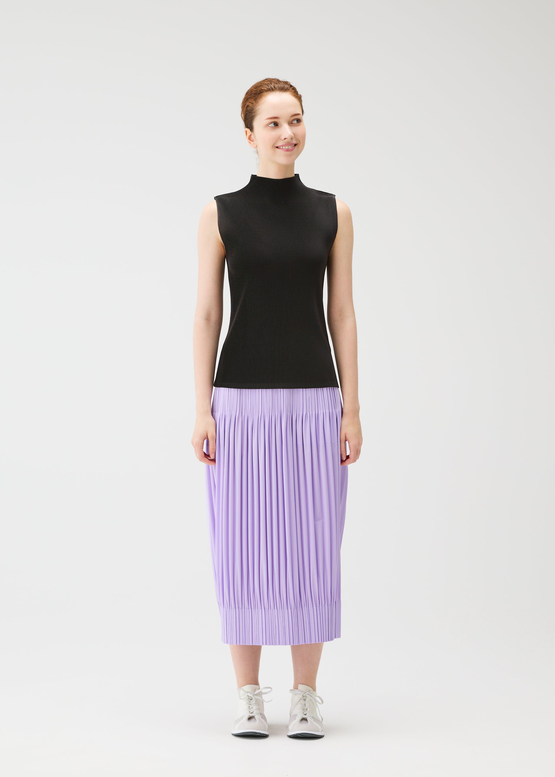 Zoomed view A woman with auburn hair and fair skin smiles to the side, wearing a black sleeveless mock-neck top paired with PLEATS PLEASE ISSEY MIYAKE’s OPAQUE BOTTOMS, a flowing purple matte-textured skirt in a relaxed silhouette.