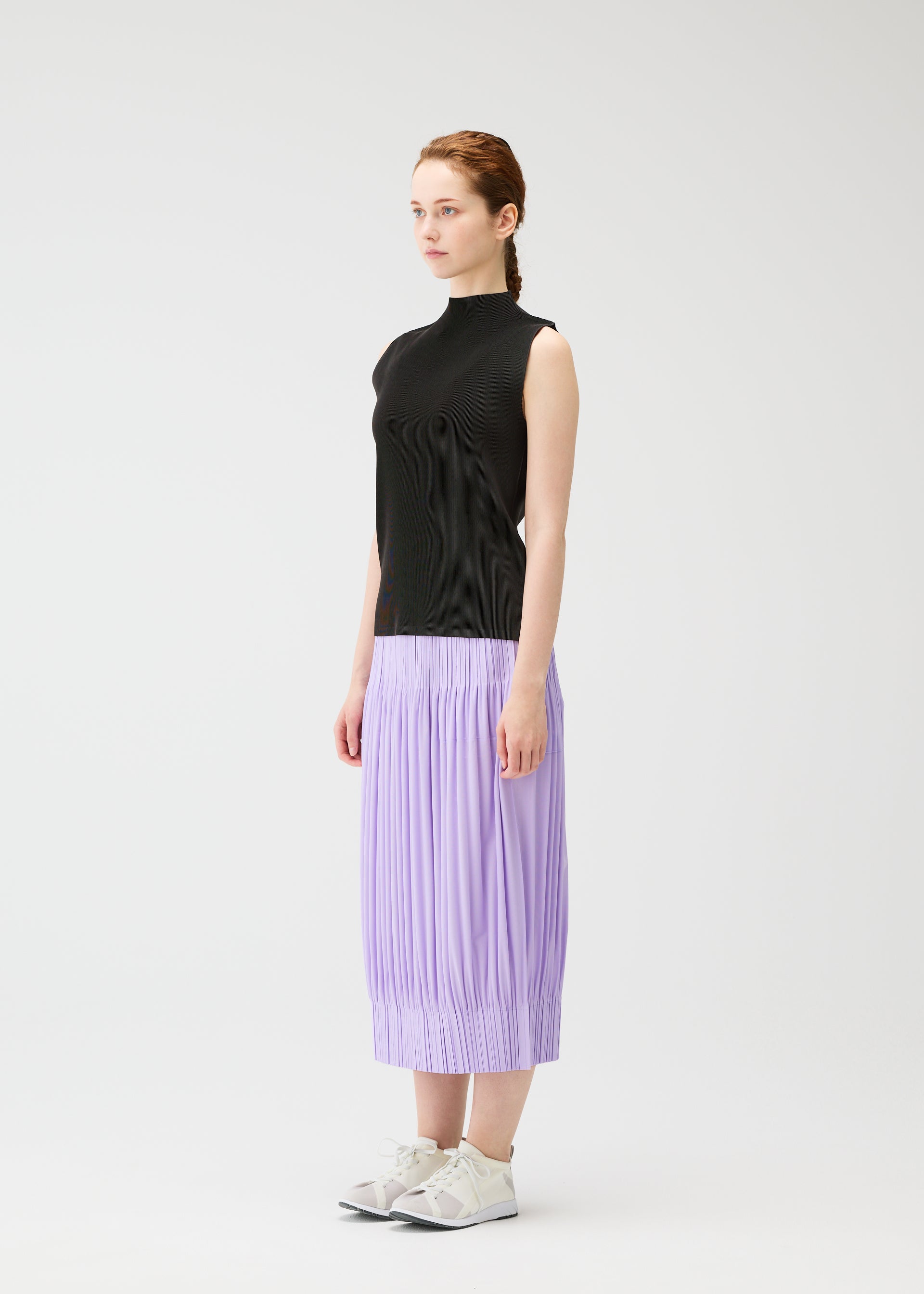 Zoomed view A woman with light skin and tied-back hair stands in profile against a white background, wearing PLEATS PLEASE ISSEY MIYAKE's OPAQUE BOTTOMS—a pleated lavender midi skirt—paired with a sleeveless black top and white sneakers.
