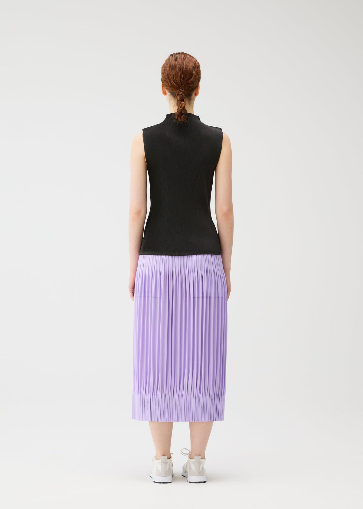 A person with braided hair, seen from behind, wears a sleeveless black top and lilac OPAQUE BOTTOMS by PLEATS PLEASE ISSEY MIYAKE, featuring pleated matte fabric and pockets, paired with white sneakers against a plain white background. view 7 of 7