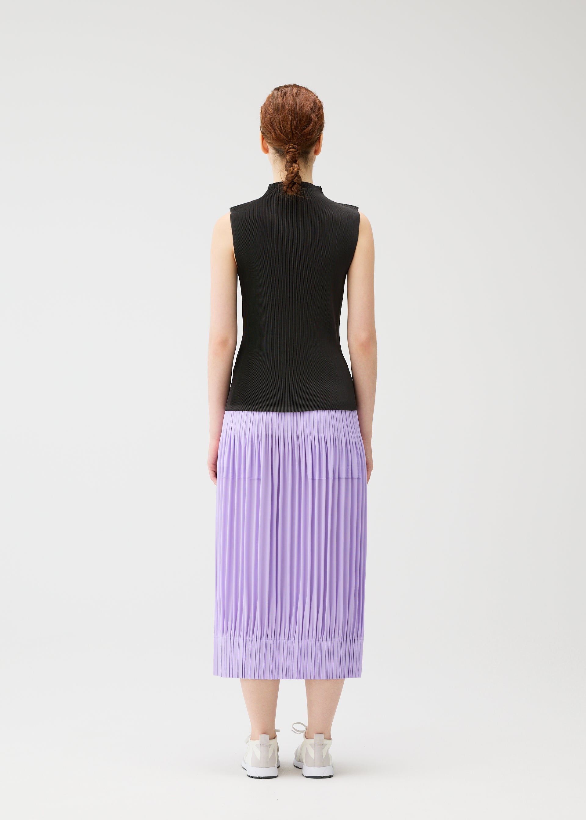 Zoomed view A person with braided hair, seen from behind, wears a sleeveless black top and lilac OPAQUE BOTTOMS by PLEATS PLEASE ISSEY MIYAKE, featuring pleated matte fabric and pockets, paired with white sneakers against a plain white background.