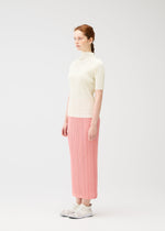 A woman with light skin and red braided hair stands sideways in a white space, wearing PLEATS PLEASE ISSEY MIYAKE’s THICKER BOTTOMS 2: a pink pleated midi skirt in fresh spring colors, paired with a cream short-sleeve top and white sneakers.